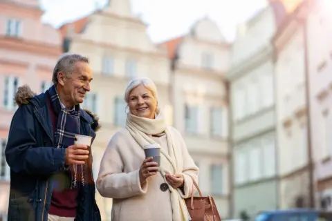 Uśmiechnięta para seniorów z kawą na spacerze. Idealne wycieczki dla seniorów samolotem, by odkrywać nowe miejsca.