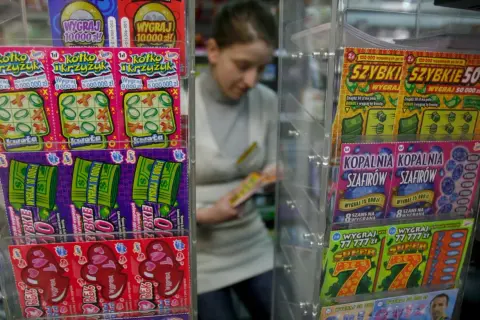 Zdrapki "Pieniądze jak lodu" i inne losy na loterii w kiosku. Kobieta wybiera zdrapkę.