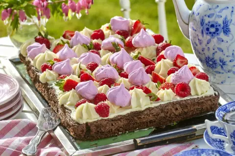 En chokladkaka i långpanna, dekorerad med grädde, maränger och färska bär. Perfekt för ett sommarfika.