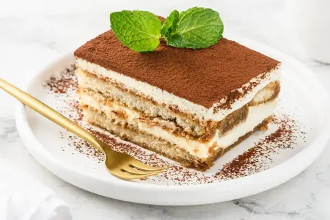Pyszny kawałek tiramisu z mascarpone, posypany kakao i udekorowany miętą. Idealny na deser.