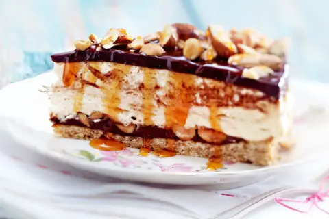 Ein Stück cremiger Käsekuchen mit Schokoladenglasur, Karamell und Nüssen als köstliches cheesecake topping.