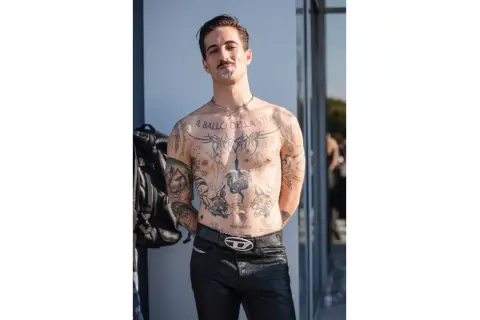 Damiano David, a torso covered in tattoos, poses confidently.