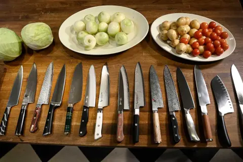 En samling vassa köksknivar ligger uppradade på en träbänk, redo att ta sig an kål, lök och tomater. Varje bra kökskniv är ett verktyg för kulinariska äventyr.