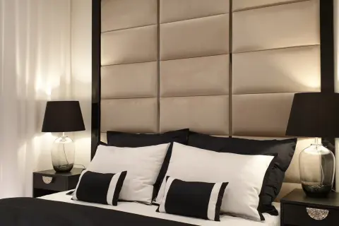 Elegancka sypialnia w stylu hotelowym. Miękkie, pikowane wezgłowie, czarno-biała pościel i stylowe lampki nocne tworzą luksusową atmosferę.