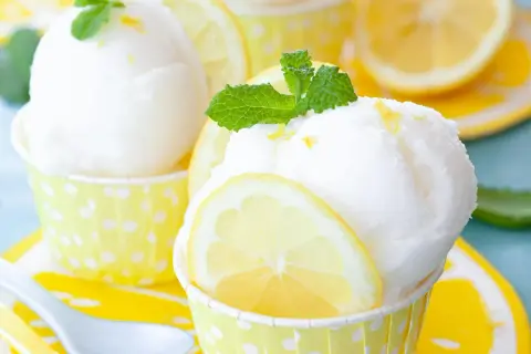 Erfrischendes Zitronensorbet-Rezept: Kugeln in gelben Tupfenförmchen, garniert mit Zitronenscheiben und Minze.