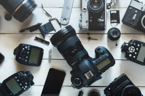 Rozłożone na białym tle aparaty fotograficzne, obiektywy i lampy błyskowe.