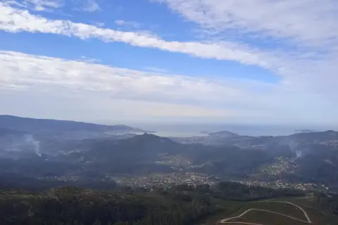 Vista panorámica desde el monte Galiñeiro, con un valle salpicado de casas y el mar al fondo bajo un cielo nublado.