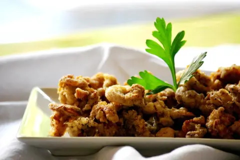 Camagroc crujiente en un plato blanco, decorado con perejil fresco. ¡Un bocado delicioso!