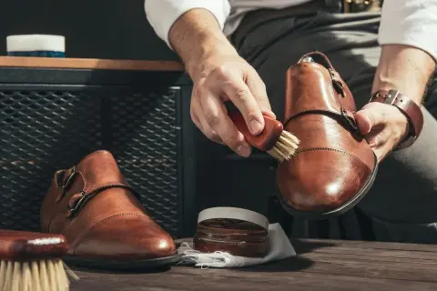 Mężczyzna czyści brązowe skórzane buty, używając szczoteczki i pasty. Dowiedz się, czym wyczyścić skórzane buty, by wyglądały jak nowe.