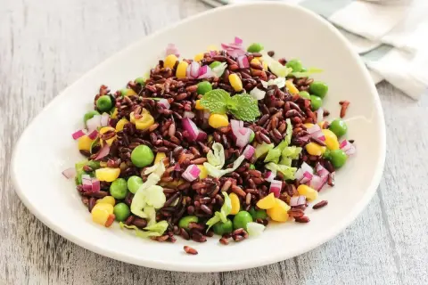 Un colorato riso venere con verdure fresche: piselli, mais, cipolla rossa e lattuga, guarnito con menta.
