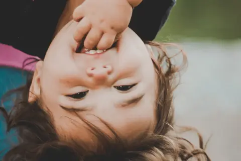 Uśmiechnięte dziecko z palcem w buzi, widać kilka mleczaków.