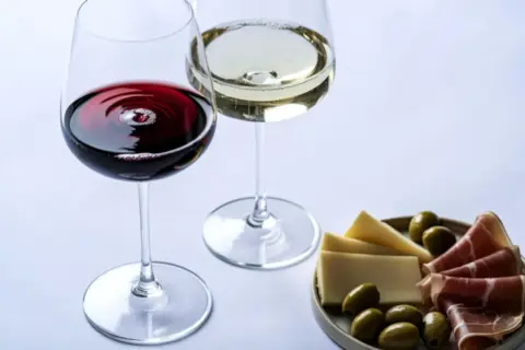 Dwa kieliszki wina, czerwonego i białego, z deską serów, oliwek i szynki. Wino właściwości są doceniane przez koneserów.