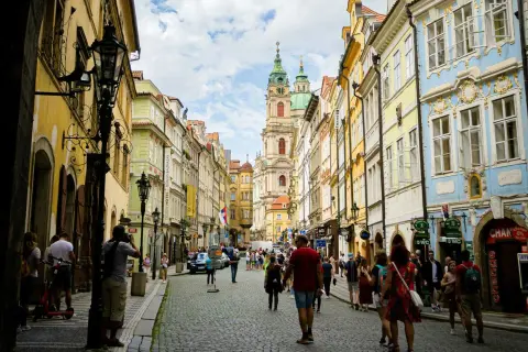 Rue pavée bordée de maisons colorées à Prague, avec une église baroque au loin. Une scène typique du top 10 des attractions de Prague.