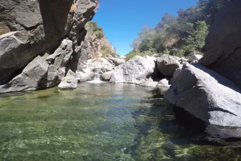 Agua cristalina en la charca de las nutrias, rodeada de rocas y vegetación bajo un cielo azul.