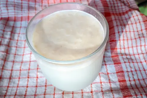 Szklanka z kremowym napojem, który może być kefir czy maślanka, stoi na czerwono-białym ręczniku.