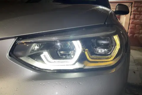 Gros plan sur un phare led qui clignote, illuminant la carrosserie mouillée d'une voiture argentée.