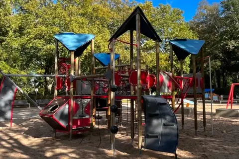 Ein bunter Spielplatz mit Klettergerüst und Schaukeln in einem der Wuppertal Parks, umgeben von Bäumen im Herbstlicht.