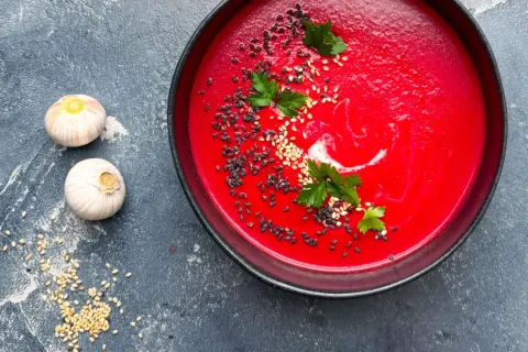 Eine leuchtend rote Bete Suppe, garniert mit Sesam und Petersilie, neben zwei Knoblauchzehen.
