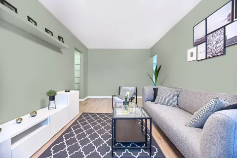 Quel mur peindre pour agrandir une pièce étroite ? Ce salon moderne aux murs vert pâle, avec un canapé gris et des cadres photos, offre une ambiance apaisante.