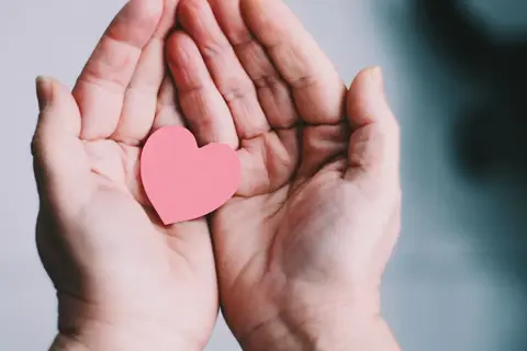 Zwei Hände halten ein rosa Herz. Ein Symbol für Geben und Nehmen, Liebe und Fürsorge.