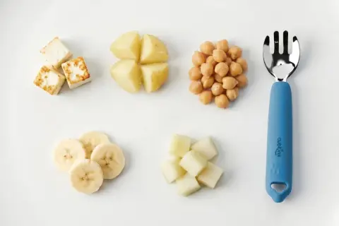 A child can eat with a fork when they master finger foods like these: paneer cubes, potato wedges, chickpeas, banana slices, and melon cubes.
