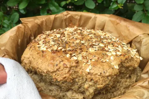 Pan de lino recién horneado, cubierto de semillas y avena, envuelto en papel de hornear.