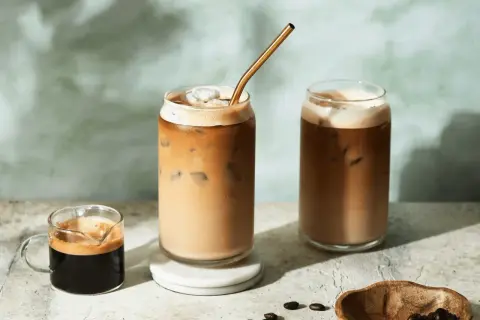 Deux verres de latte froid avec une paille dorée, un petit shot d'espresso et des grains de café.