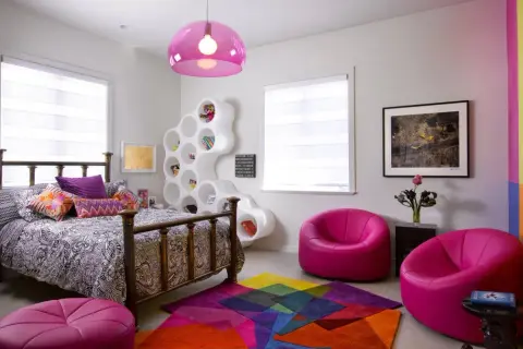 Habitación moderna y colorida, ideal para decorar con estilo. Cama con dosel, estantería blanca escultural, alfombra geométrica y sillones fucsia.