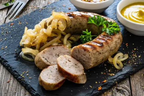 Pyszna biała kiełbasa z grilla, podana z duszonymi cebulkami i musztardą. Idealna na letni obiad.