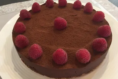 Tarte chocolat framboise, une gourmandise visuellement irrésistible, saupoudrée de cacao et ornée de framboises fraîches.