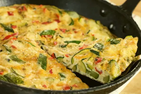 Pyszny omlet z cukinii z kawałkami papryki, podany na patelni. Idealny na śniadanie lub lekki obiad.