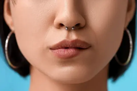 Kobieta z septum w nosie i kolczykami w uszach na niebieskim tle.