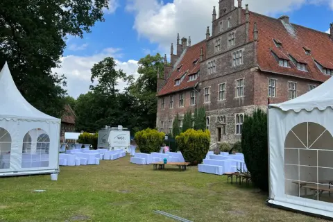 Festzelt und weiße Sitzreihen vor historischem Gebäude. Ein Anbieter für Eventausstattung hat hier alles für ein Fest vorbereitet.