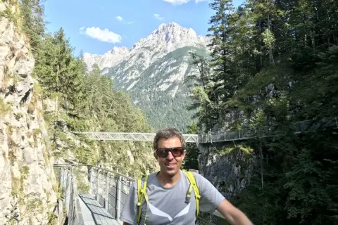 Mann auf einem Steg in der Leutascher Geisterklamm, umgeben von Felsen und Bäumen, mit majestätischen Bergen im Hintergrund.