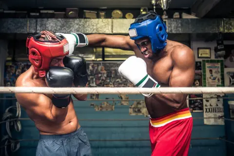 Två boxare i ringen, en med röd och en med blå hjälm, tränar funktionell fitness.