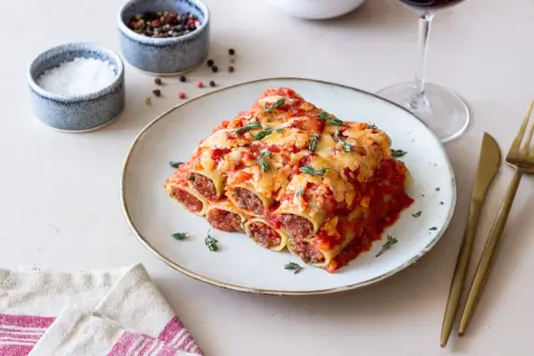 Pyszne cannelloni z mięsem mielonym, zapieczone pod sosem pomidorowym i serem, udekorowane świeżym tymiankiem.