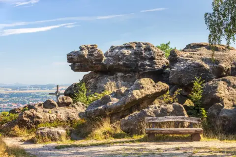 Ein Holzbank lädt zum Verweilen ein, mit Blick auf bizarre Felsen im Zittauer Gebirge und eine Stadt in der Ferne.