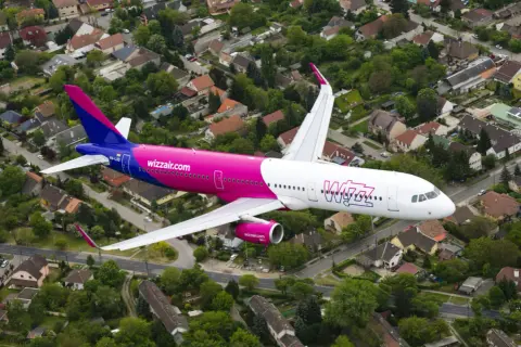 Różowy samolot Wizzair przelatuje nad osiedlem domów jednorodzinnych.