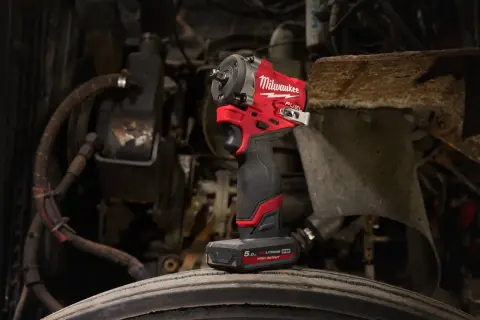 Czerwony klucz udarowy Milwaukee M12 FUEL stoi na oponie, gotowy do pracy przy silniku.