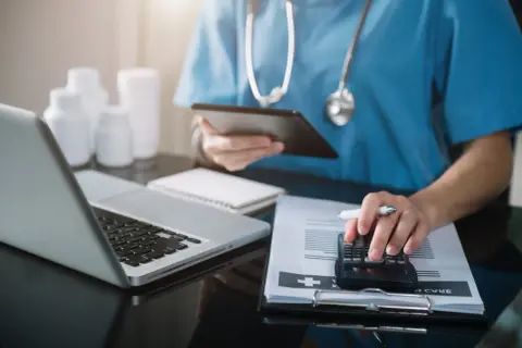 Lekarz analizuje dokumentację medyczną i rachunki, korzystając z kalkulatora i tabletu. Rozliczenia usług medycznych VAT.