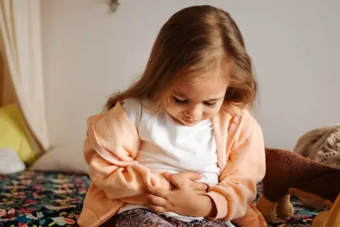 Litet barn med magsjuka och feber håller sig om magen.