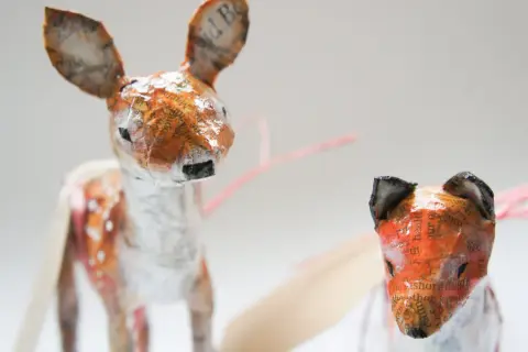 Urocze figurki z papier mache: jelonek w plamki i lis. Ich uszy zdobią fragmenty tekstu.