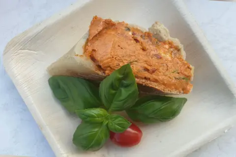 Ein Stück Brot mit leckerer Tomatenbutter, garniert mit frischem Basilikum und einer Kirschtomate. Perfekt zum Tomatenbutter selber machen.