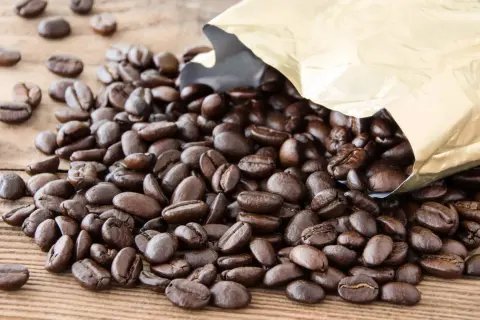 Chicchi di caffè Arabica tostati, con un sacchetto dorato aperto da cui fuoriescono. Il caffè Arabica, noto per il suo aroma delicato, è il significato di un'esperienza gustativa raffinata.