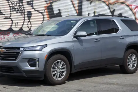 Szary Chevrolet Traverse SUV zaparkowany przed ścianą z graffiti.