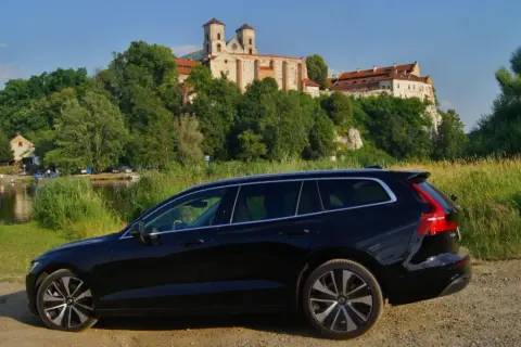 Czarne Volvo V60 na tle malowniczego klasztoru i rzeki. Idealne na wakacyjne podróże, gdzie niskie volvo v60 spalanie pozwoli cieszyć się widokami.