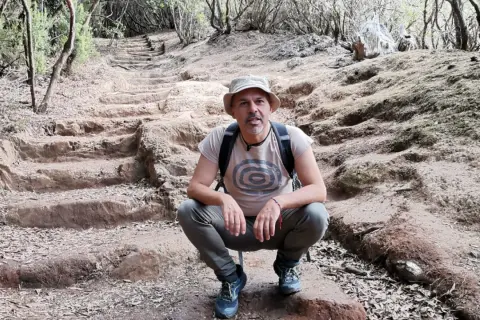 Hombre con sombrero y mochila en el sendero de los sentidos Tenerife, rodeado de vegetación y escalones de tierra.