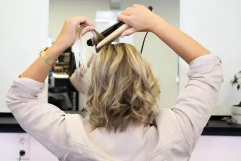 Frau stylt ihre Haare mit einem Glätteisen, um sanfte Wellen zu kreieren.