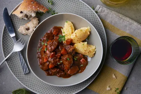 Herzhaftes Spezzatino di manzo mit cremigem Polenta, dazu ein Glas Rotwein und rustikales Brot.