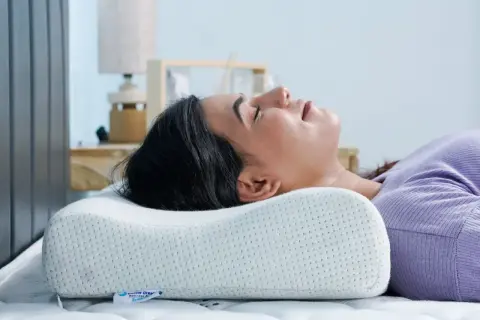 Woman sleeping on her back with head cradled by an ergonomic pillow, demonstrating the **forma correcta de dormir con almohada** for optimal neck support.